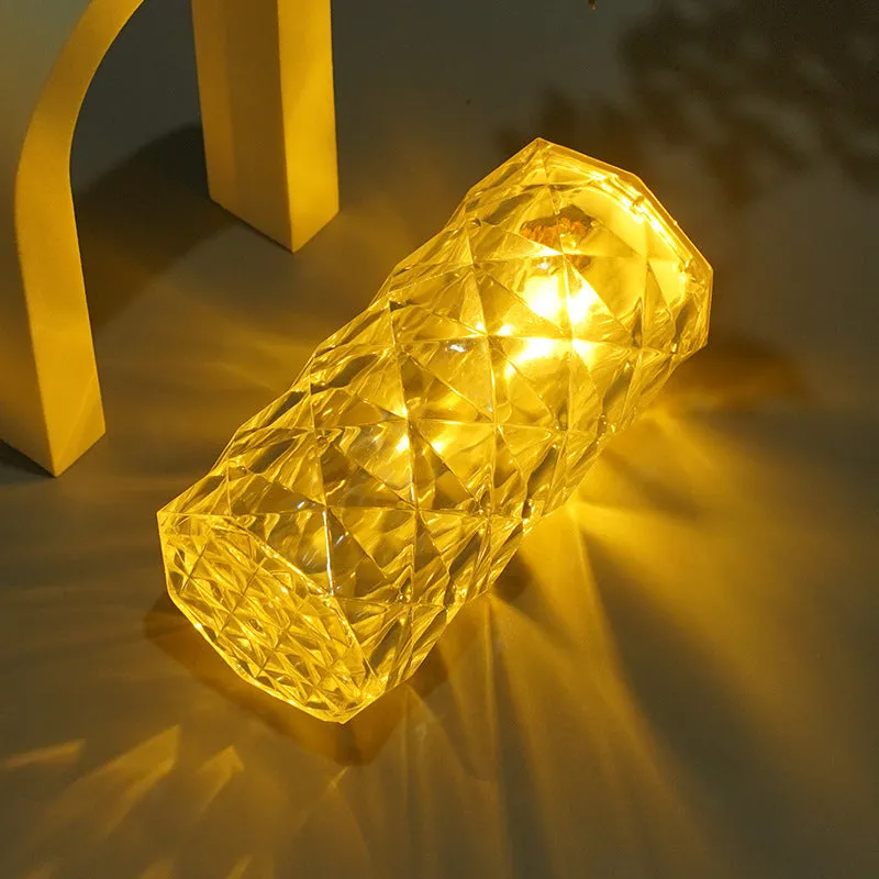 Rose atmosphere crystal bedside lamp with plastic lampshade emitting soft yellow light on a wooden table