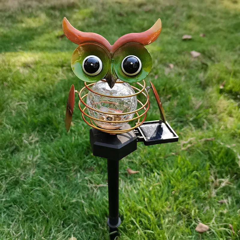 Solar-powered owl lawn lamp with iron sculpture and glass lampshade in a garden setting