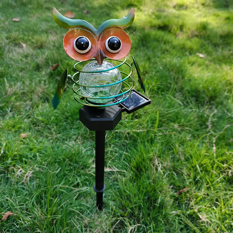 Solar-powered owl lawn lamp with iron sculpture and glass lampshade in a garden setting