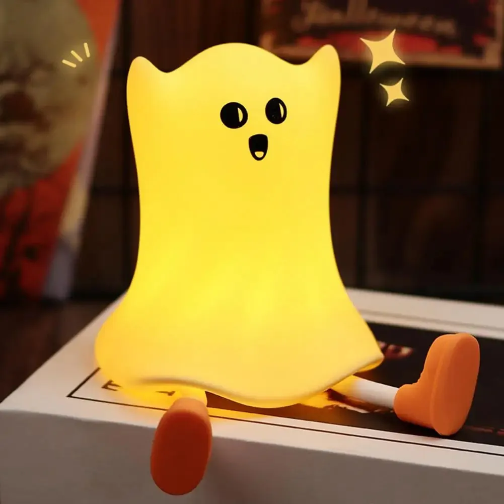 Ghost shaped silicone bedside lamp with touch control emitting soft yellow glow on a bedside table