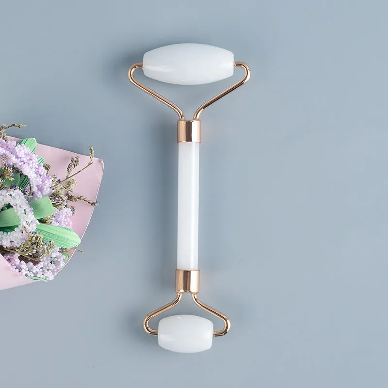 White jade facial roller with double heads and a matching gua sha scraping board on a plain surface.