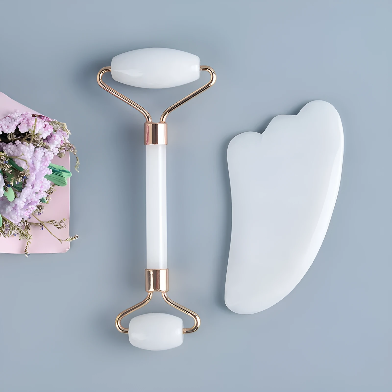 White jade facial roller with double heads and a matching gua sha scraping board on a plain surface.