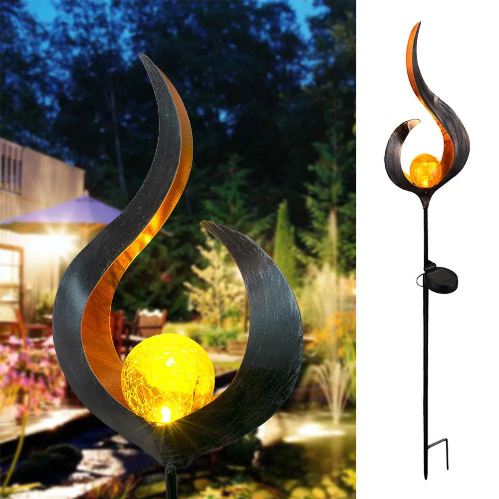 LED solar flame light with warm white glow in a garden, featuring iron and glass construction and stake stand