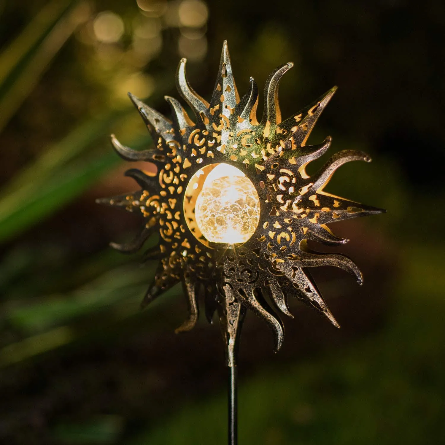 LED solar flame light with warm white glow in a garden, featuring iron and glass construction and stake stand