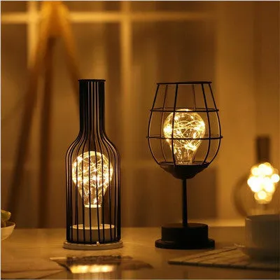 Hollow wrought iron wine bottle shaped table lamp with warm white LED light on a wooden desk