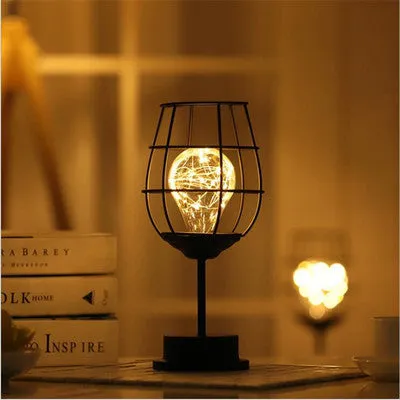 Hollow wrought iron wine bottle shaped table lamp with warm white LED light on a wooden desk