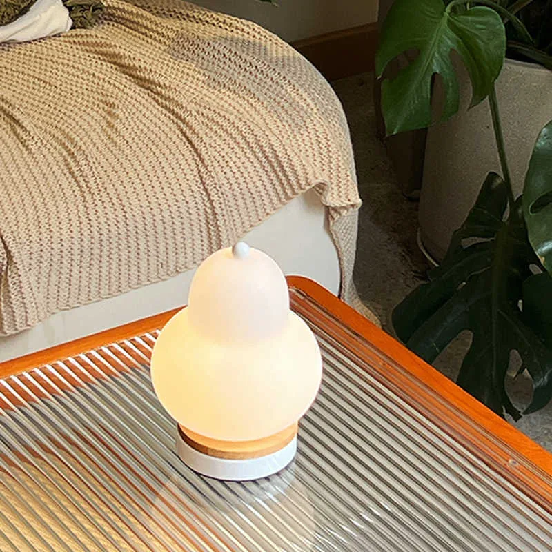 White pear-shaped rechargeable touch LED table lamp with PE shade on a wooden bedside table