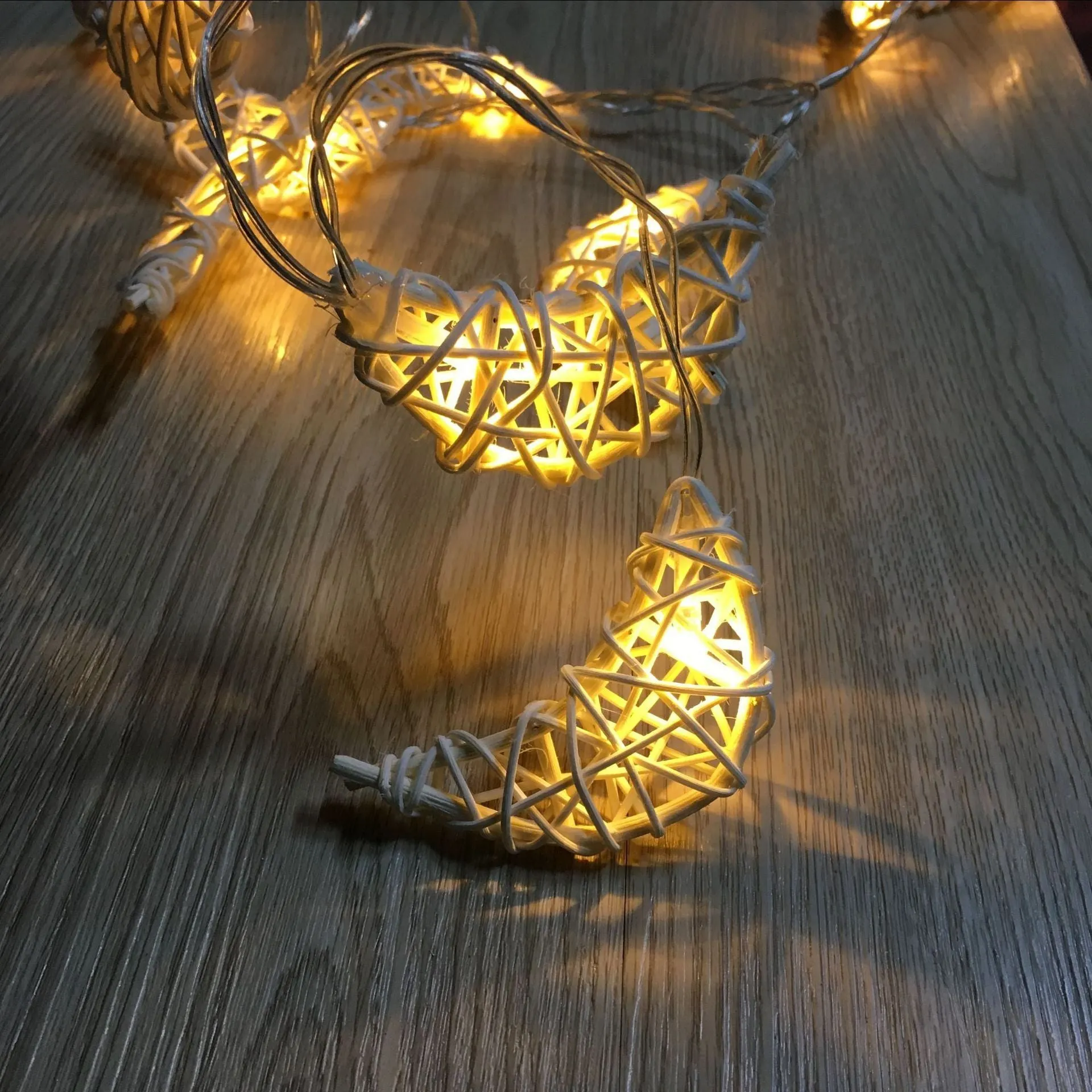 Handwoven rattan moon pendant fairy light chain with warm white glow on a dark background