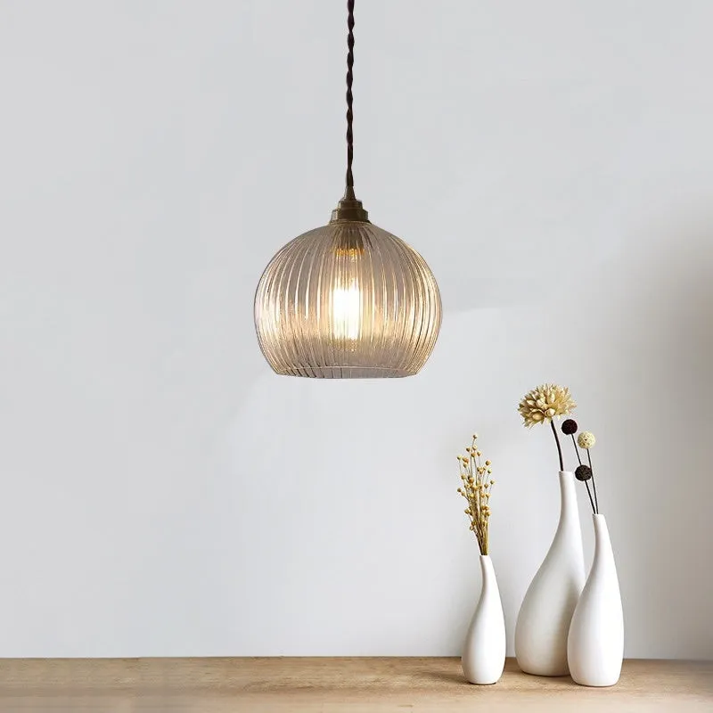 Minimal single head pendant lamp with copper body and transparent glass shade on a dark background