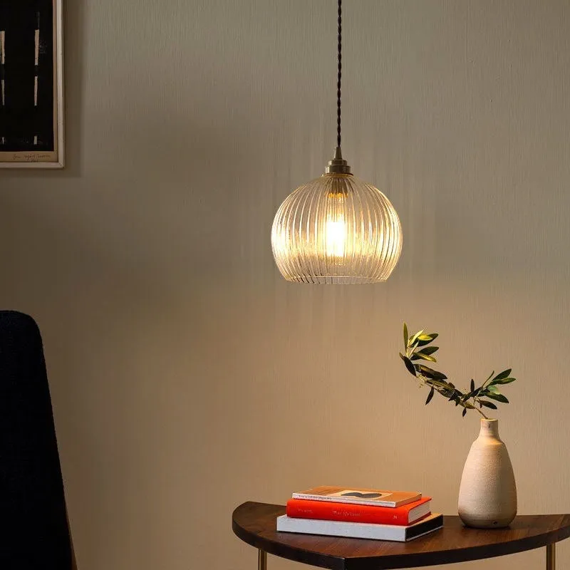 Minimal single head pendant lamp with copper body and transparent glass shade on a dark background