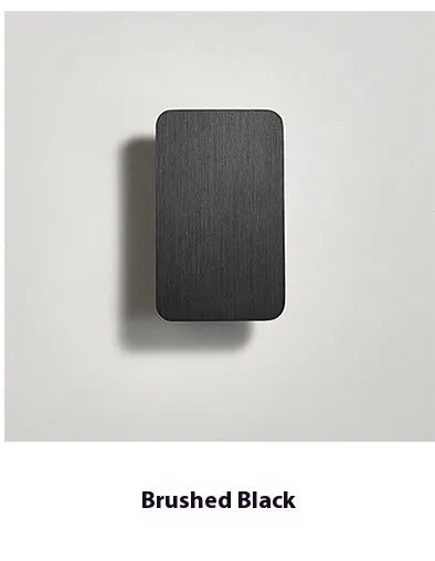 Minimalist black nordic wall lamp mounted beside a bed, emitting warm white light.
