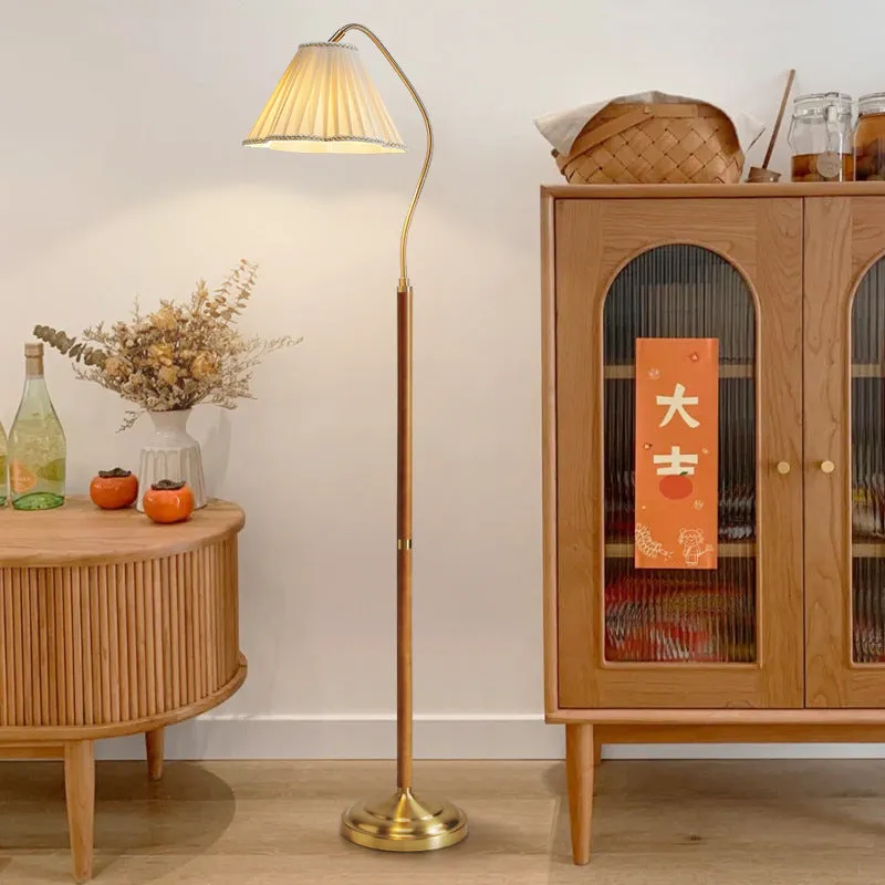 Solid wood floor lamp with fabric shade in walnut colour placed beside a sofa in a living room