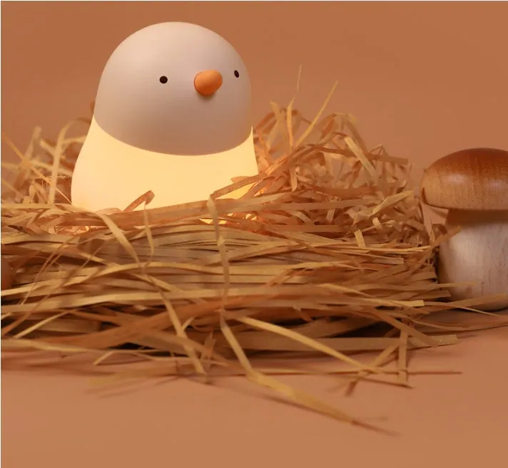 Pecking rice chicken small night light with warm yellow glow on a wooden bedside table, USB charging cable visible