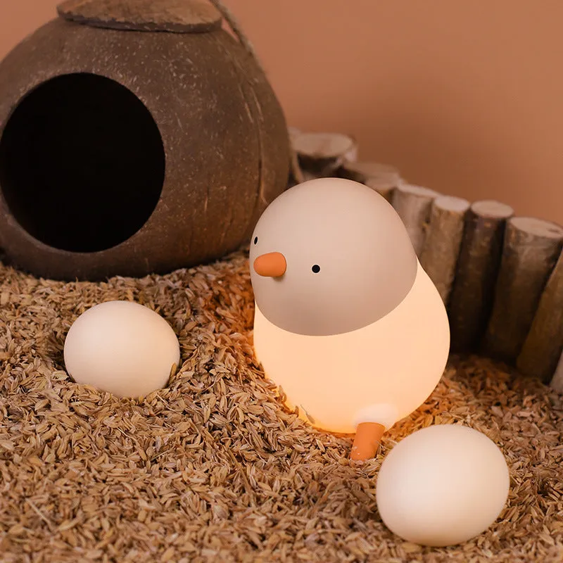 Pecking rice chicken small night light with warm yellow glow on a wooden bedside table, USB charging cable visible