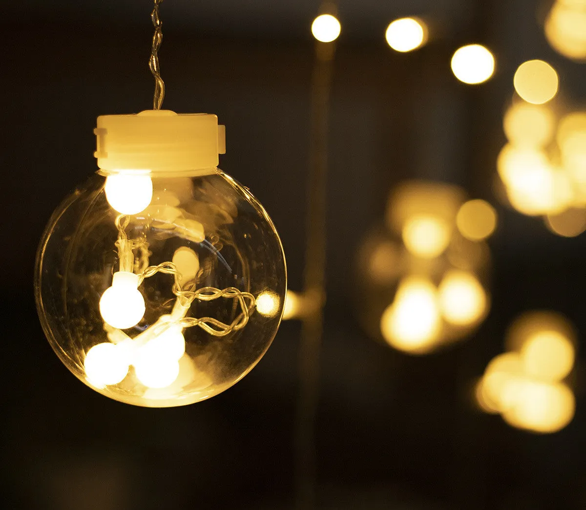 2.5 metre 108 LED curtain light string in warm white mode on a dark background showing plastic shell and plug-in cable