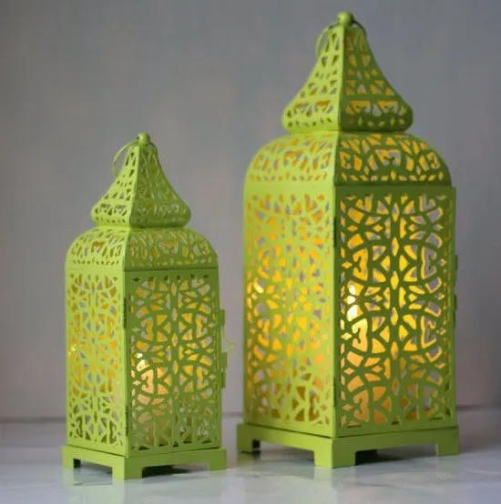 A blue iron Moroccan lantern candlestick with a hollow geometric design, shown next to a white and yellow pair.