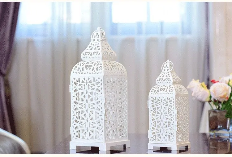 A blue iron Moroccan lantern candlestick with a hollow geometric design, shown next to a white and yellow pair.