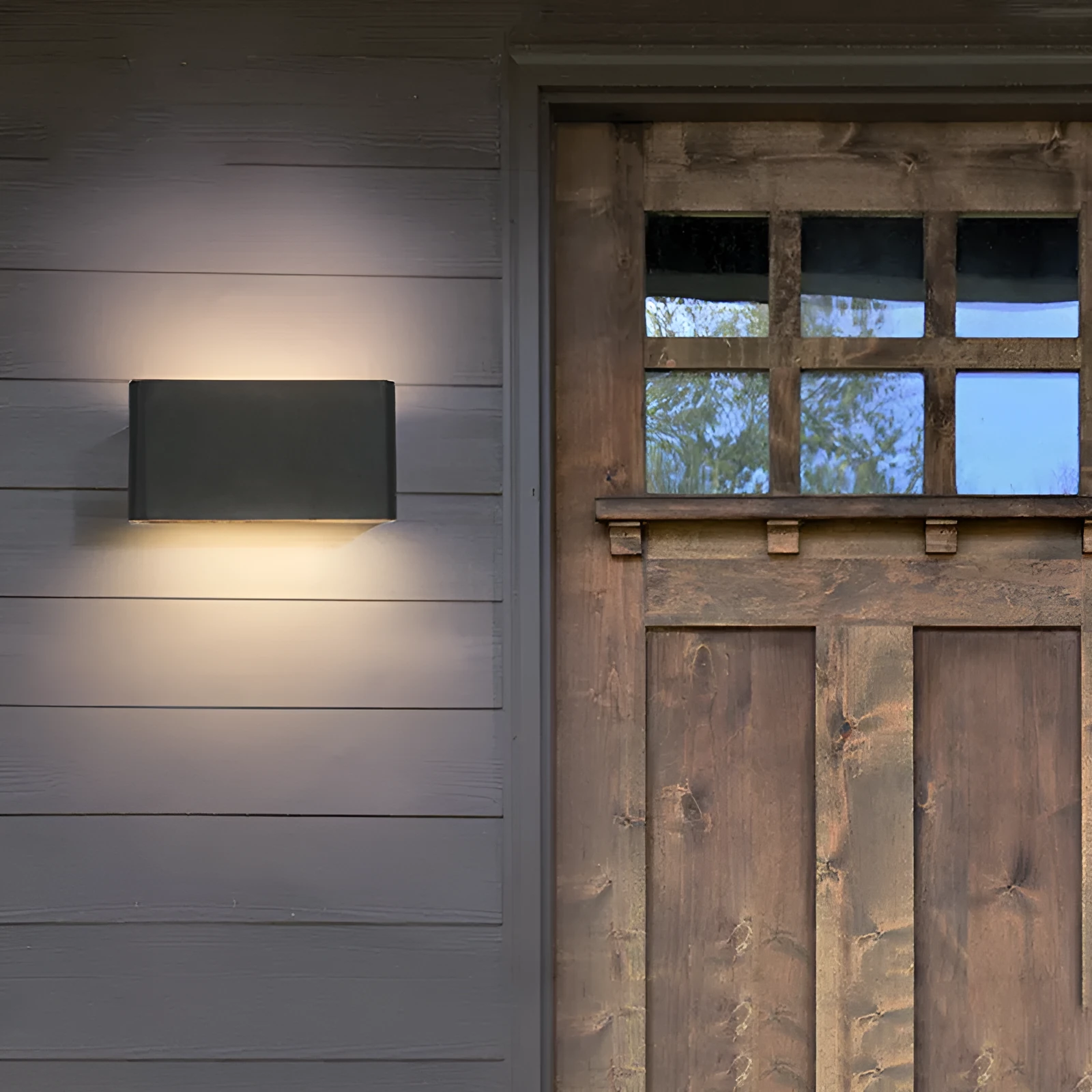 Rectangular LED outdoor wall lamp in black finish with warm light on a brick courtyard wall