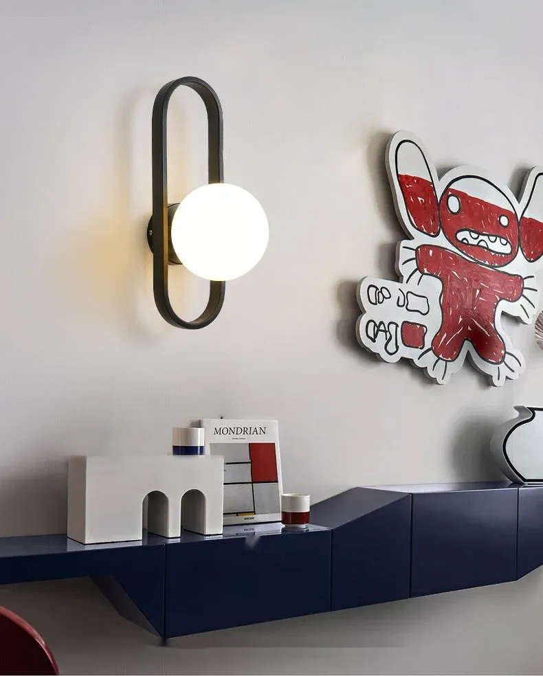 Minimalist wall-mounted lamp with clear glass bulb shade on a black iron sconce arm and backplate.