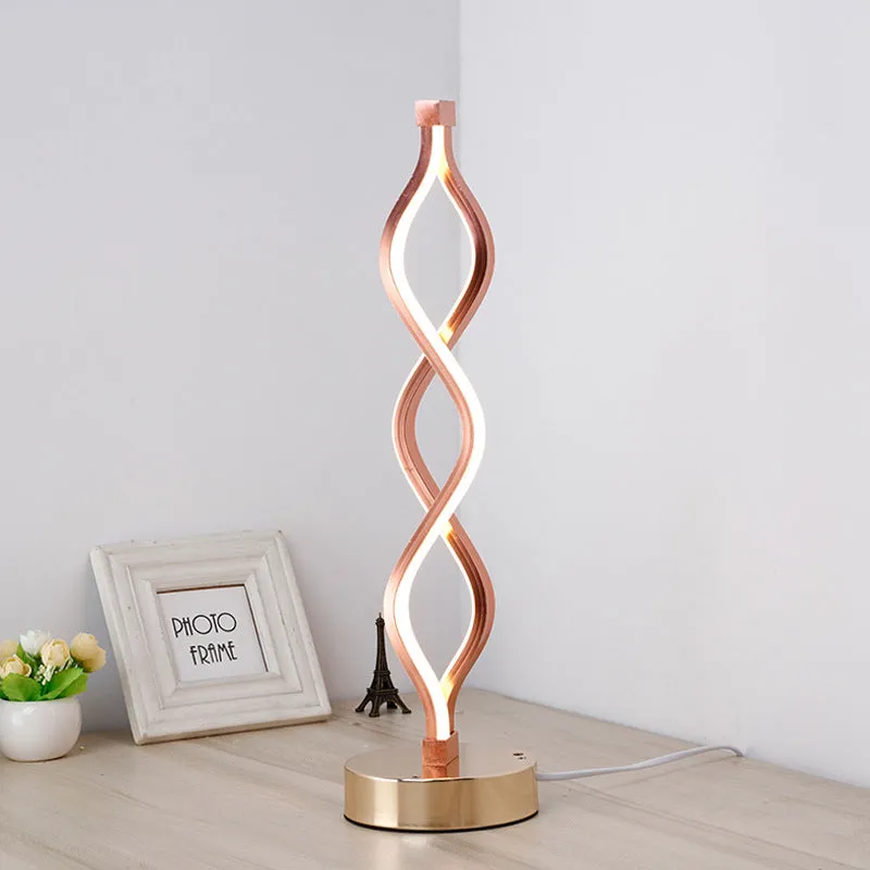 Modern LED desk lamp with aluminium metal body and acrylic mask, gold colour, on a desk