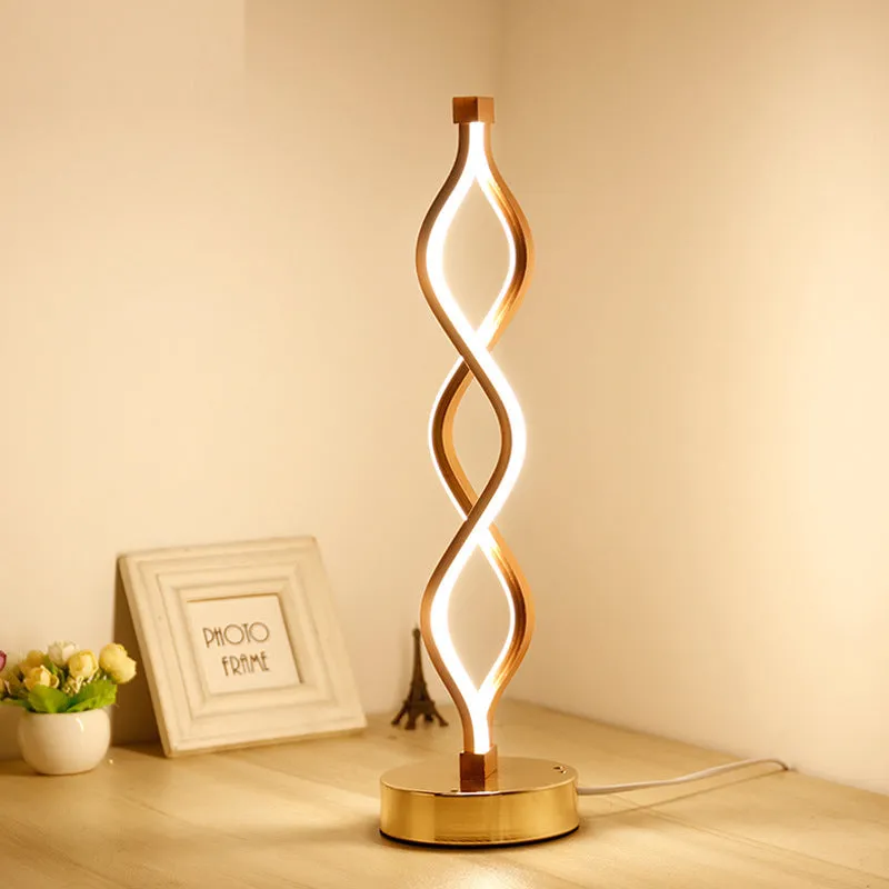 Modern LED desk lamp with aluminium metal body and acrylic mask, gold colour, on a desk