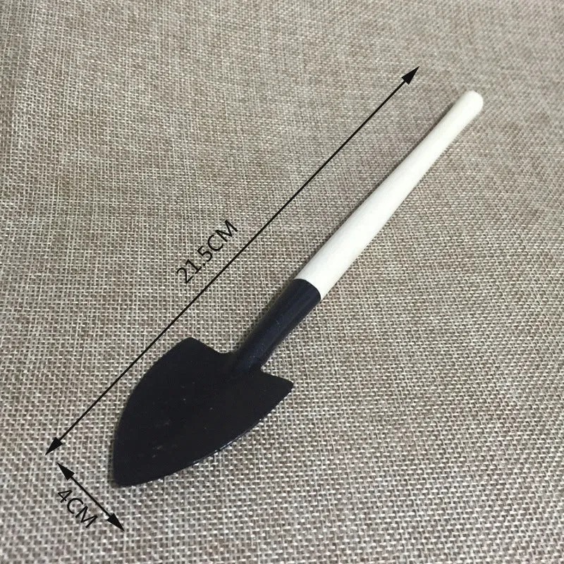 Succulent gardening tool set showing a small watering can, bucket, mini shovel, rake, tweezers, and scissors on a table.