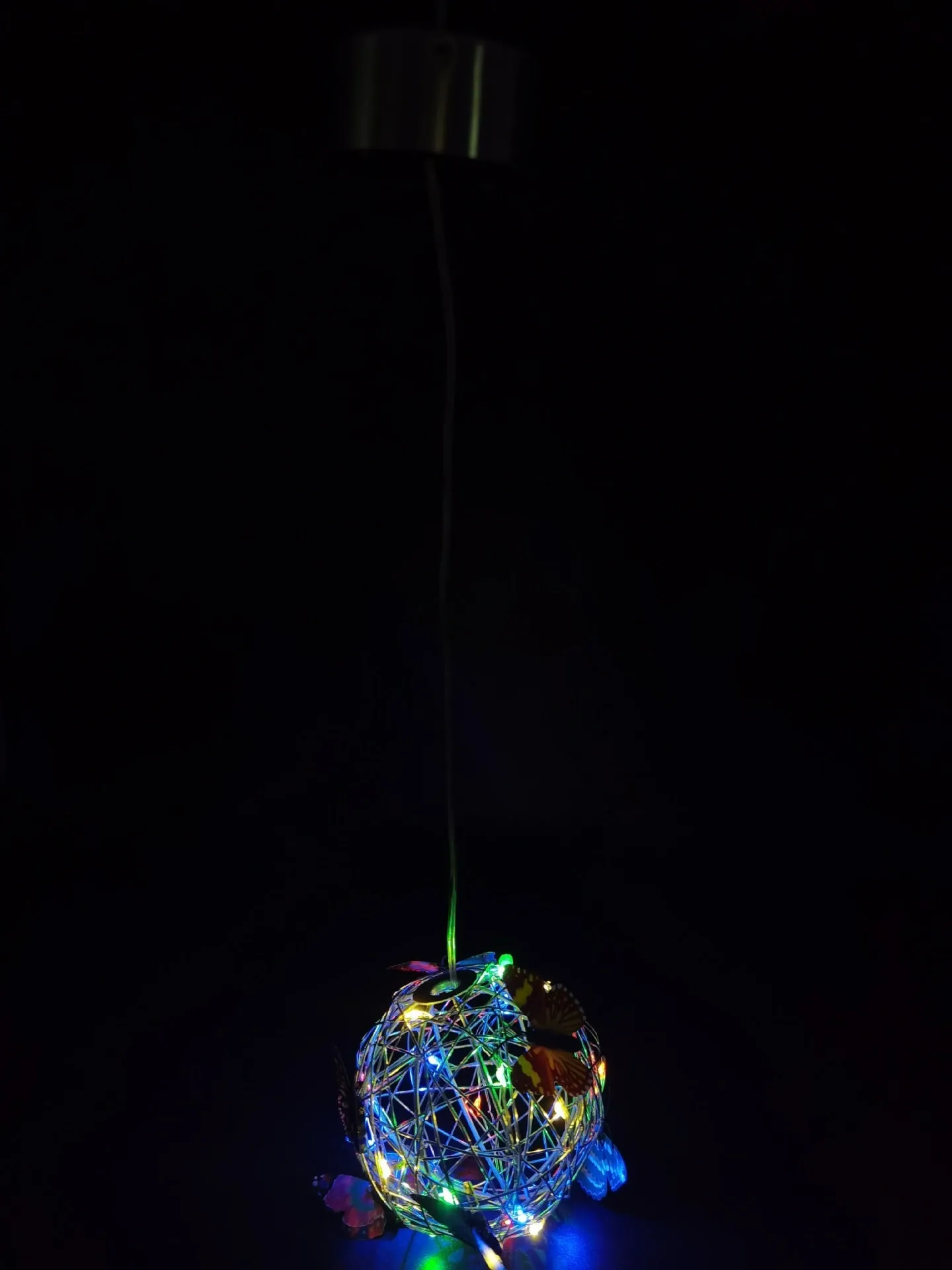 White outdoor solar ball light with random colour butterfly decorations on a garden lawn