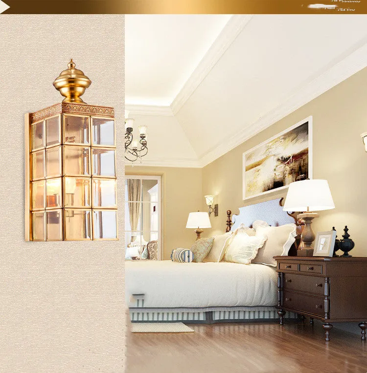 Full copper wall lamp with glass shade and gold finish on a brick balcony wall