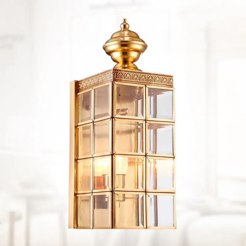 Full copper wall lamp with glass shade and gold finish on a brick balcony wall