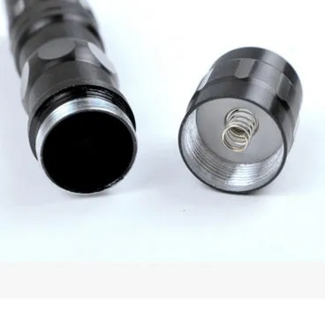 Black aluminium mini LED flashlight showing scale next to a AA battery.
