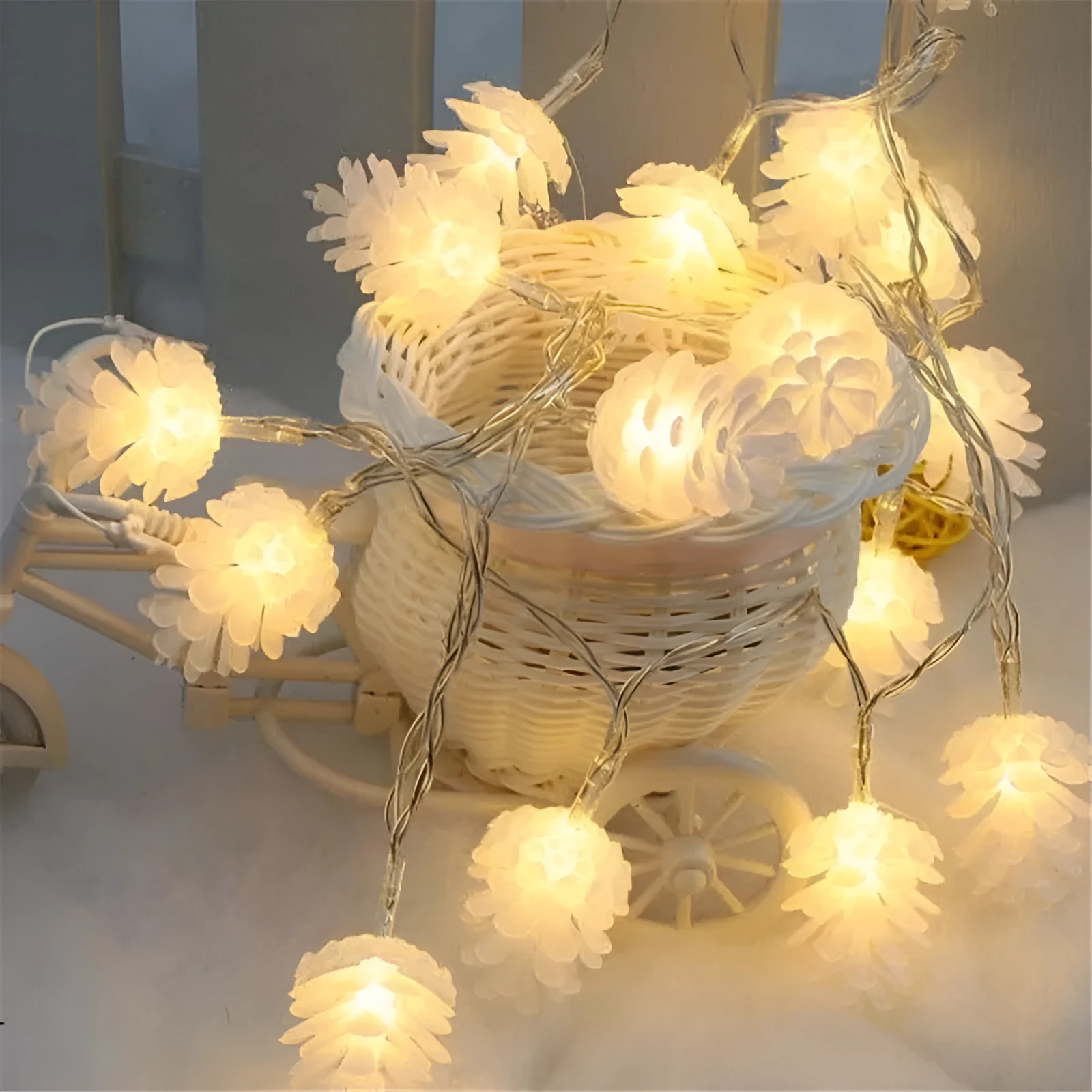 Warm white LED pine cone decorative light string powered by batteries on a green foliage background.