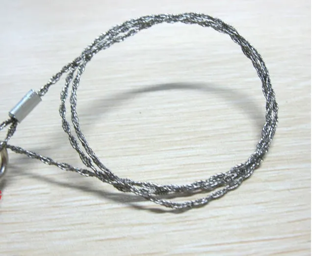 Coiled stainless steel survival wire saw with two black thumb rings, shown next to a ruler showing its 55cm length.