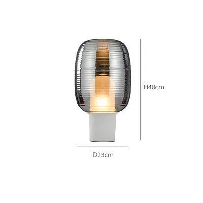 Simple modern glass table lamp on a table, shown in cognac and smoky grey colour options.