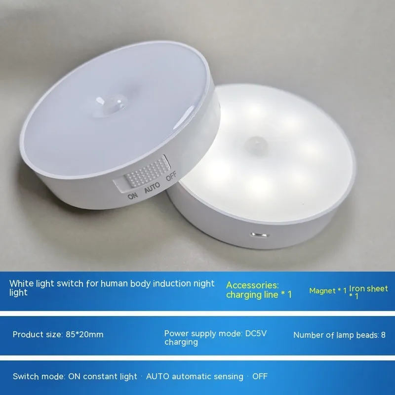 Compact white LED motion sensor night light with USB charging cable on a dark surface.