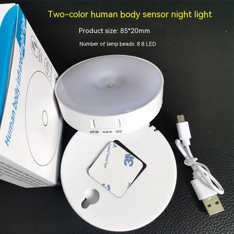 Compact white LED motion sensor night light with USB charging cable on a dark surface.