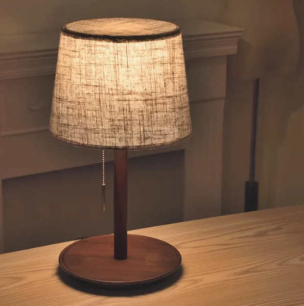 Walnut coloured solid wood bedside lamp with a white fabric lampshade and a cable switch