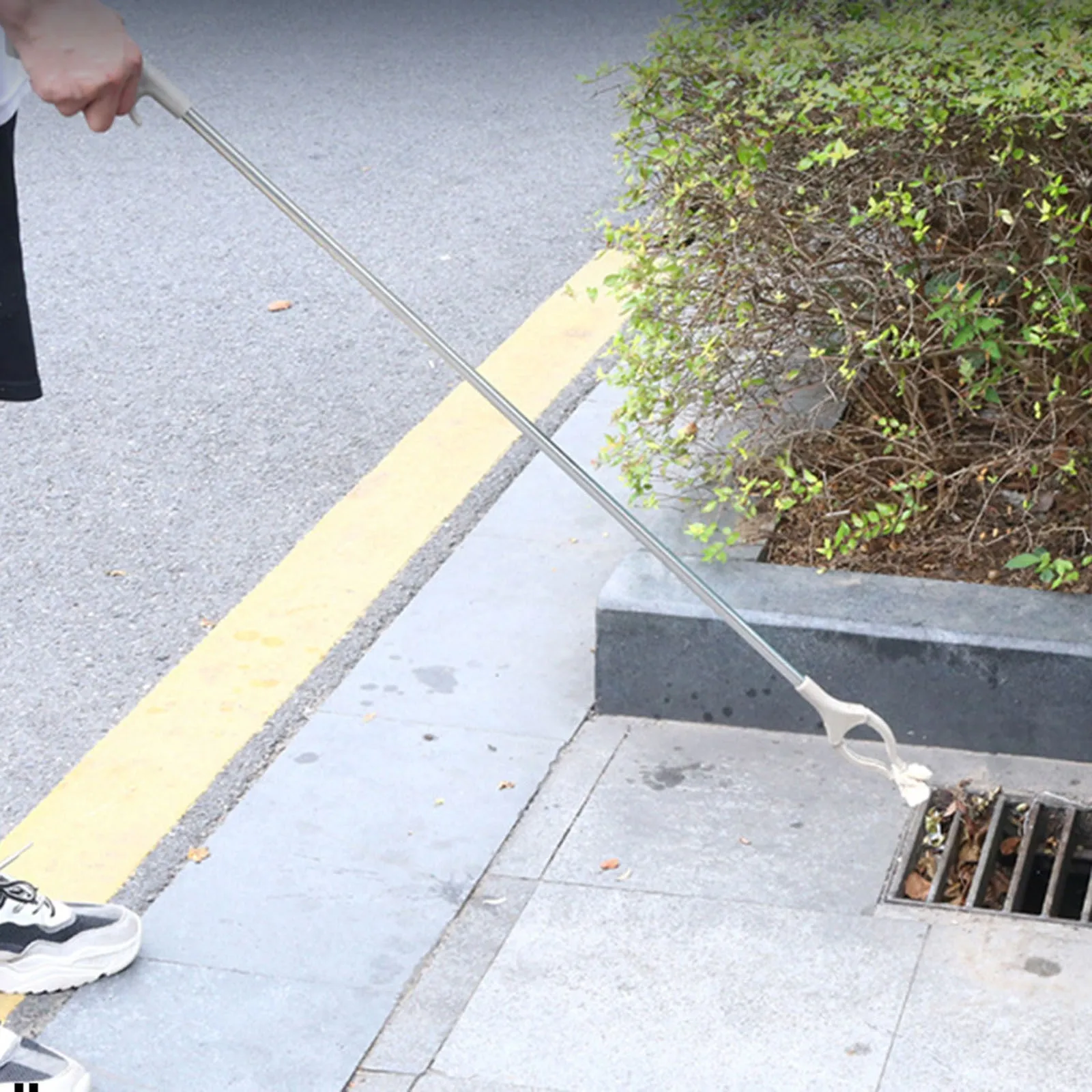 Stainless steel and plastic extended garbage picker tool with push handle and gripper jaws.