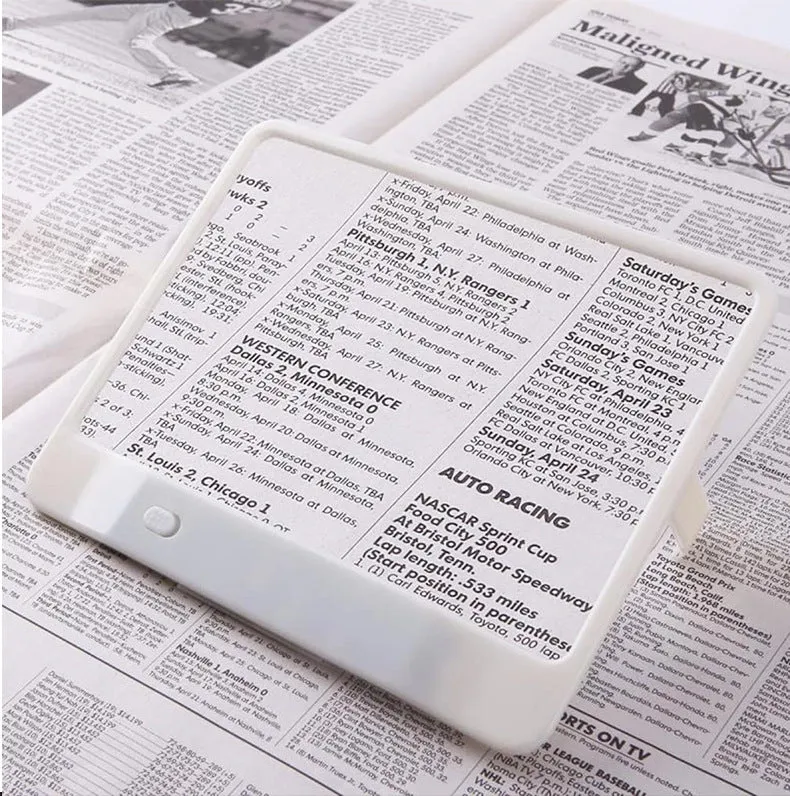 Black or white magnifying glass with integrated LED reading lamp, showing 180x140mm size and 3x magnification lens.
