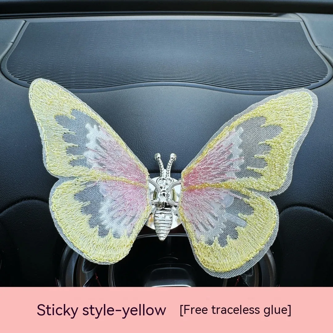 Soft fabric embroidered butterfly car air vent decoration in multiple colour options on a centre console.