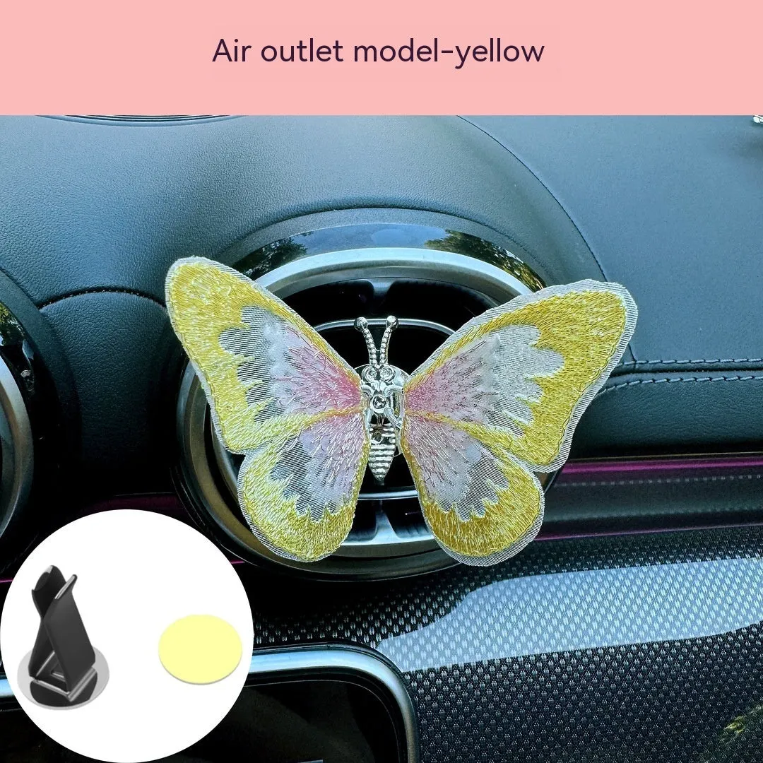 Soft fabric embroidered butterfly car air vent decoration in multiple colour options on a centre console.