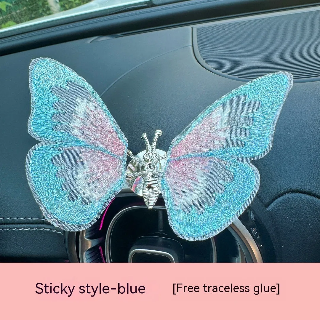 Soft fabric embroidered butterfly car air vent decoration in multiple colour options on a centre console.