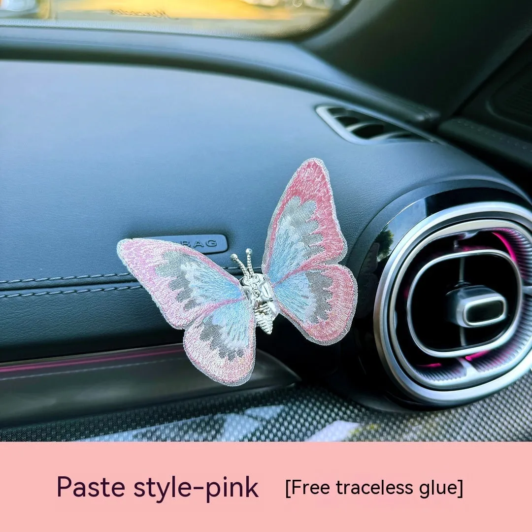 Soft fabric embroidered butterfly car air vent decoration in multiple colour options on a centre console.