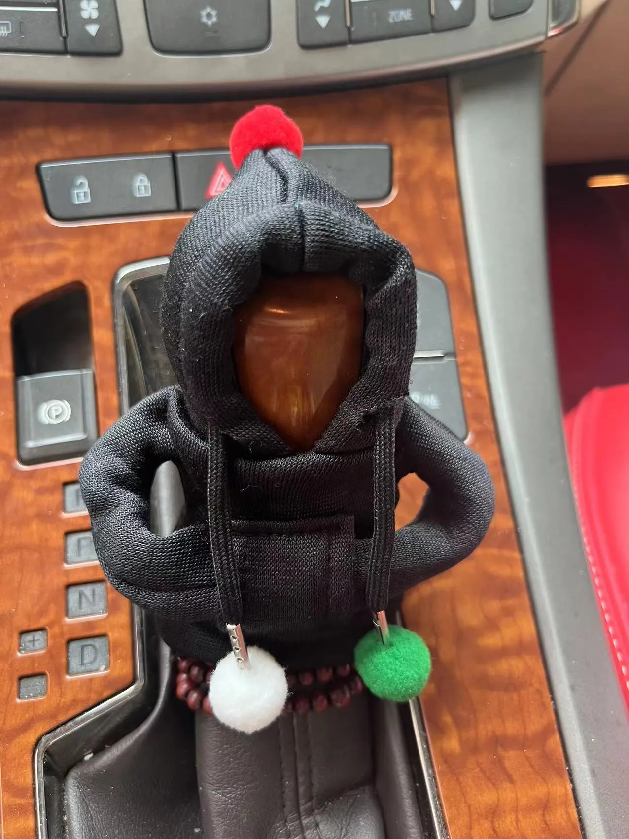 Red cloth hooded sweater cover on a car gear lever, showing decorative fur ball style.