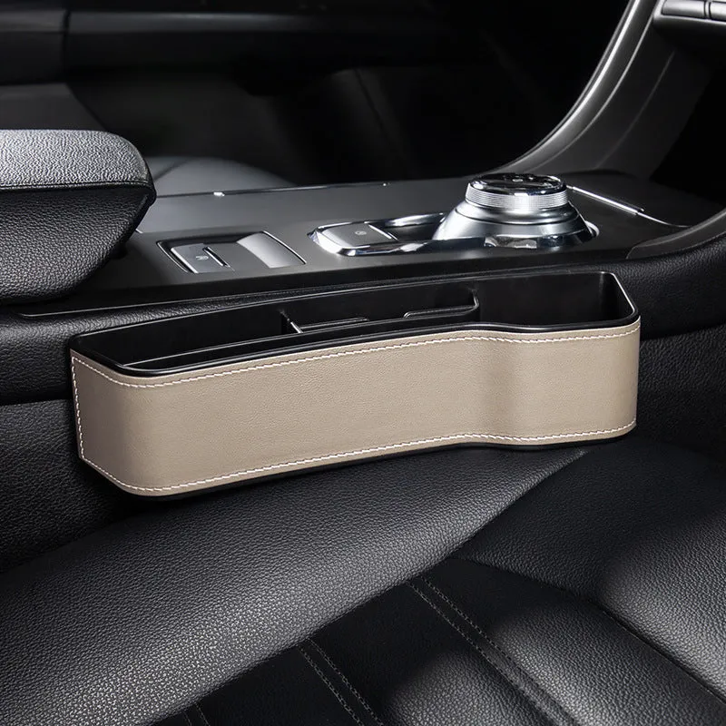 Black leather-style car seat gap storage box with cup holder and USB cable inserted between driver seat and centre console