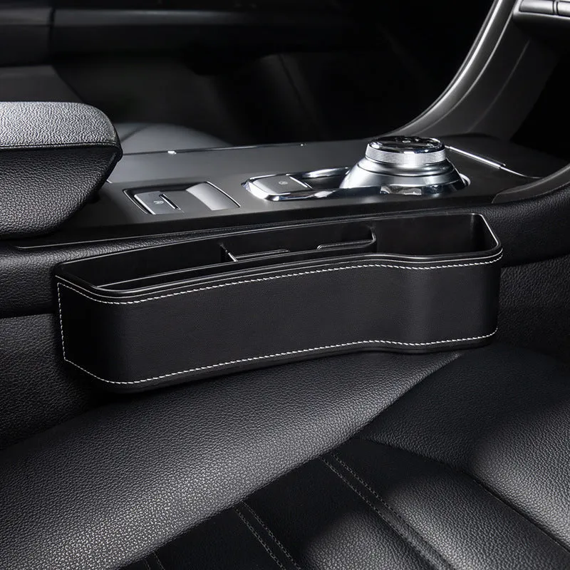 Black leather-style car seat gap storage box with cup holder and USB cable inserted between driver seat and centre console