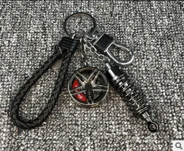 Silver metal wheel and shock absorber keychain with black braided rope and waist buckle on a white surface