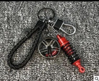 Silver metal wheel and shock absorber keychain with black braided rope and waist buckle on a white surface