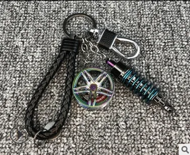 Silver metal wheel and shock absorber keychain with black braided rope and waist buckle on a white surface