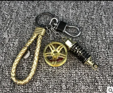 Silver metal wheel and shock absorber keychain with black braided rope and waist buckle on a white surface