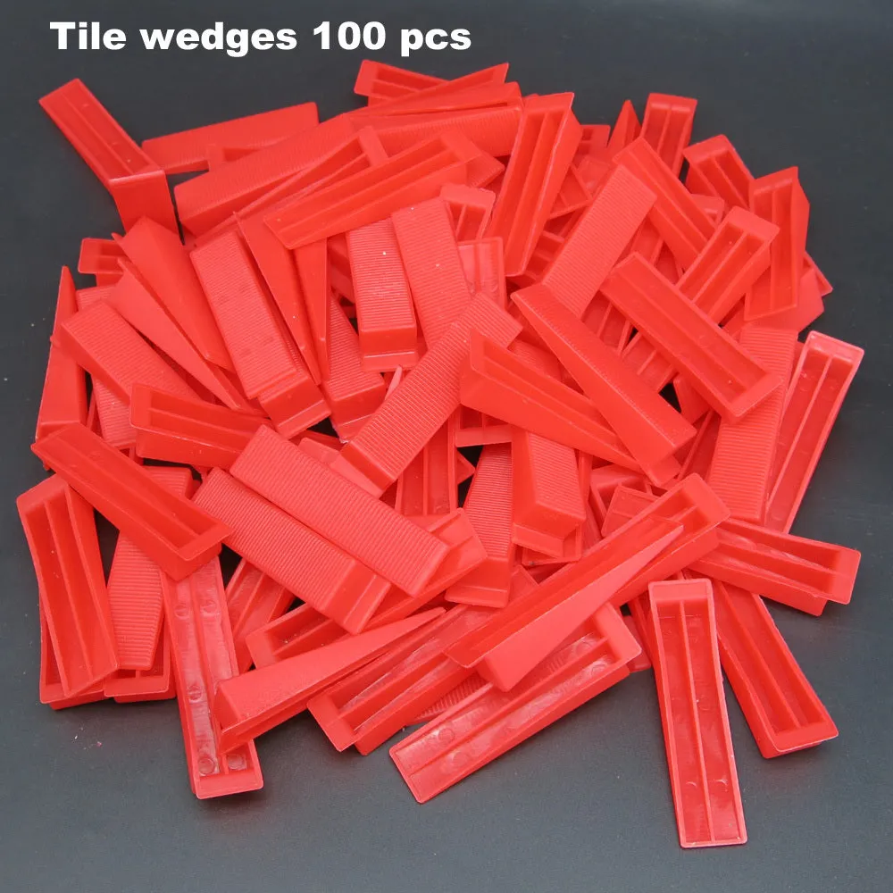 Orange plastic tile leveling wedges and white base clips on a tiled floor, with a rubber hammer nearby